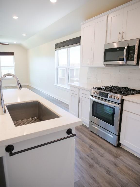 kitchen featuring vaulted ceiling, sink, white cabinets, decorative backsplash, and stainless steel appliances