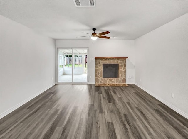 unfurnished living room featuring a stone fireplace, dark hardwood / wood-style floors, and ceiling fan