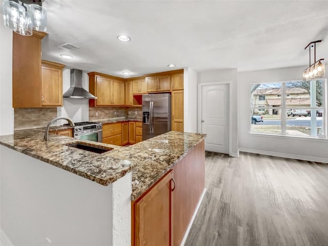 kitchen featuring stainless steel appliances, tasteful backsplash, stone countertops, kitchen peninsula, and wall chimney exhaust hood