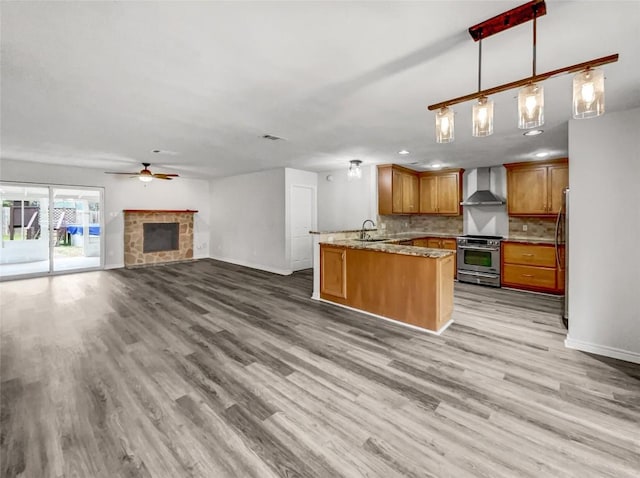 kitchen featuring hanging light fixtures, light stone counters, kitchen peninsula, stainless steel appliances, and wall chimney exhaust hood