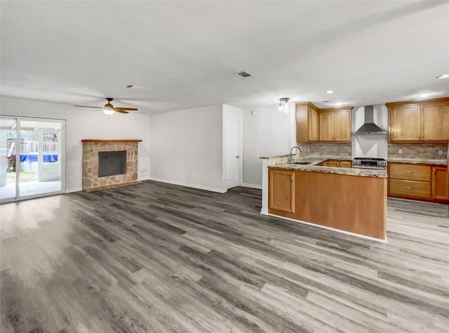 kitchen featuring sink, kitchen peninsula, a fireplace, hardwood / wood-style floors, and wall chimney range hood