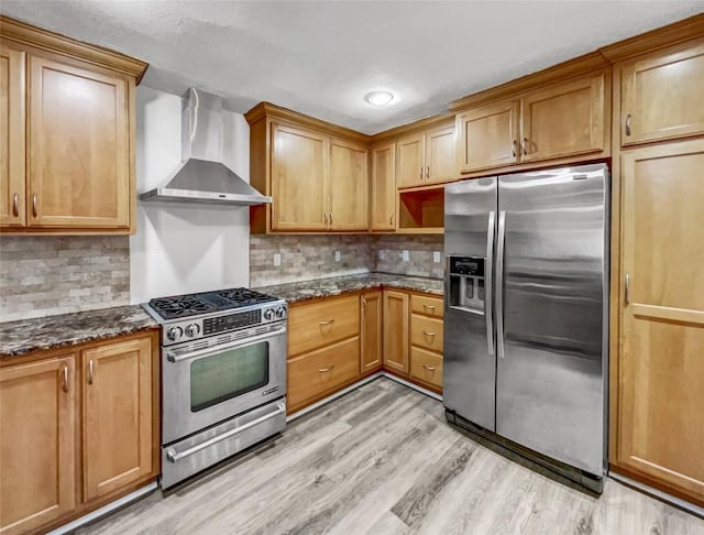 kitchen with appliances with stainless steel finishes, wall chimney range hood, decorative backsplash, and dark stone counters