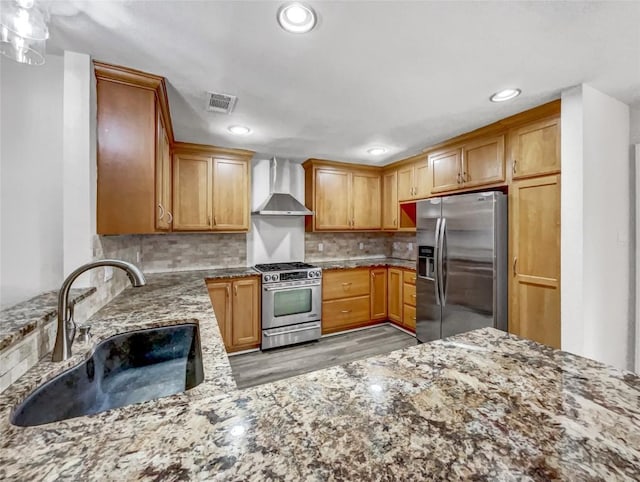 kitchen with sink, backsplash, stainless steel appliances, light stone counters, and wall chimney exhaust hood