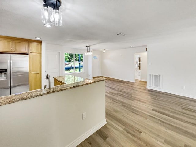 kitchen featuring stainless steel fridge with ice dispenser, light wood-style flooring, baseboards, and light stone counters