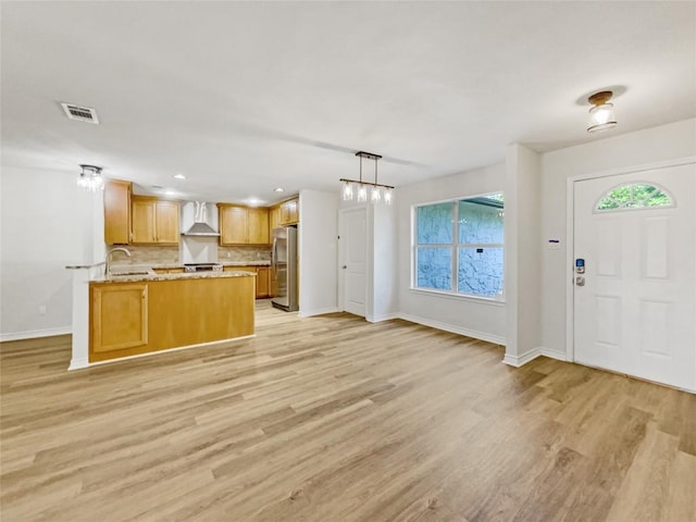 kitchen featuring freestanding refrigerator, wall chimney exhaust hood, open floor plan, baseboards, and light wood finished floors