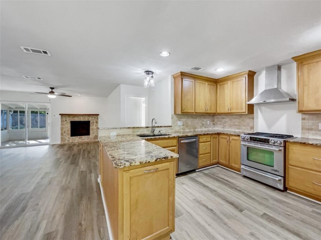 8222 Kearsarge Dr, Austin, TX 78745 - kitchen with appliances with stainless steel finishes, wall chimney exhaust hood, a sink, a peninsula, and light wood-type flooring