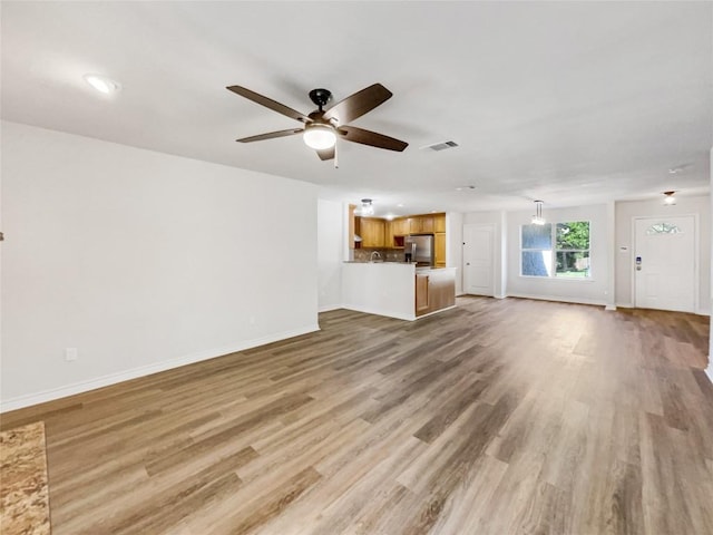 unfurnished living room with ceiling fan, light wood-type flooring, and baseboards