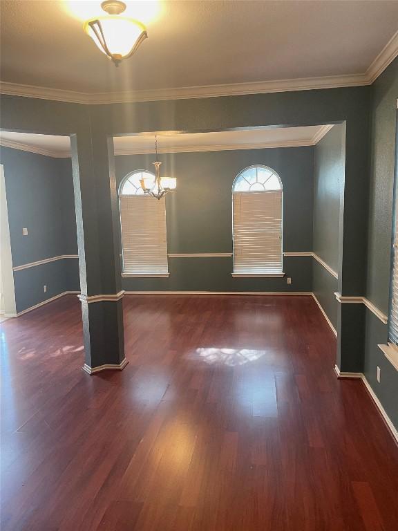 empty room with crown molding, a healthy amount of sunlight, dark hardwood / wood-style floors, and a notable chandelier