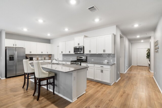 kitchen with appliances with stainless steel finishes, a kitchen island with sink, sink, and white cabinets