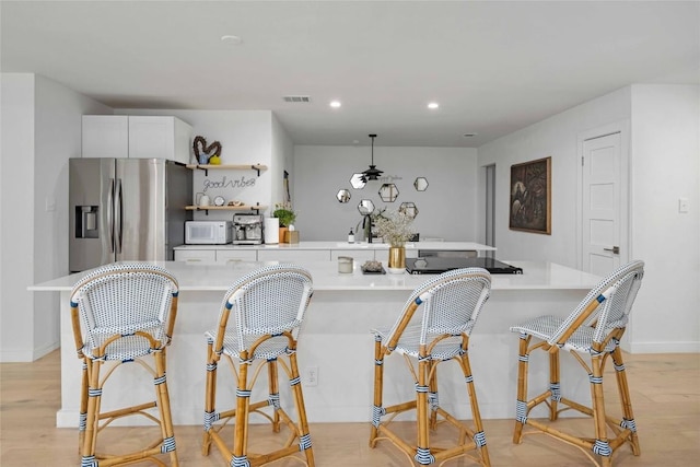 kitchen featuring light hardwood / wood-style floors, stainless steel refrigerator with ice dispenser, white cabinets, and a kitchen bar