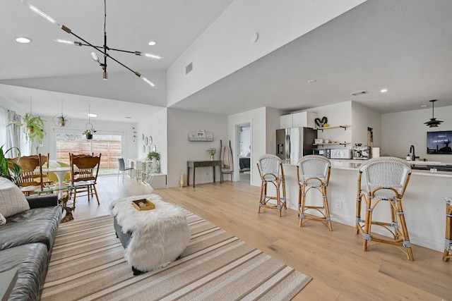 living room with lofted ceiling, an inviting chandelier, and light hardwood / wood-style flooring