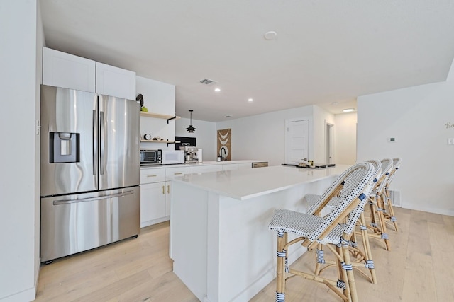 kitchen featuring stainless steel refrigerator with ice dispenser, light wood-type flooring, a kitchen island, and white cabinets