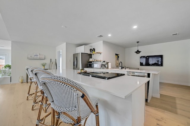 kitchen featuring white cabinetry, hanging light fixtures, light hardwood / wood-style flooring, appliances with stainless steel finishes, and kitchen peninsula