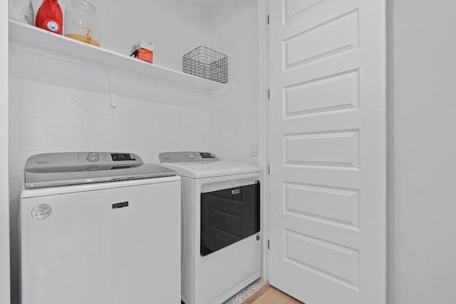 laundry area with washing machine and clothes dryer and light wood-type flooring