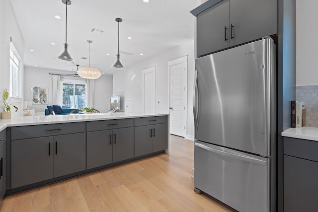 kitchen with gray cabinetry, decorative light fixtures, stainless steel fridge, and light hardwood / wood-style flooring