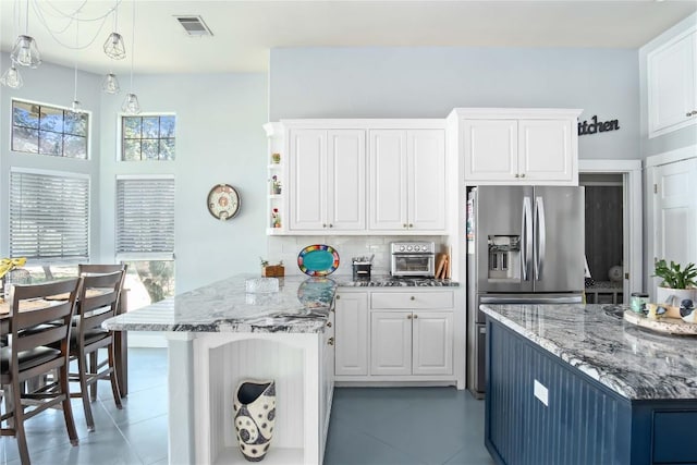 kitchen with backsplash, hanging light fixtures, light stone counters, white cabinets, and stainless steel fridge with ice dispenser