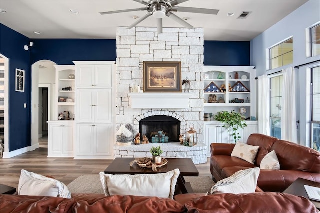 living room featuring hardwood / wood-style flooring, ceiling fan, and a stone fireplace