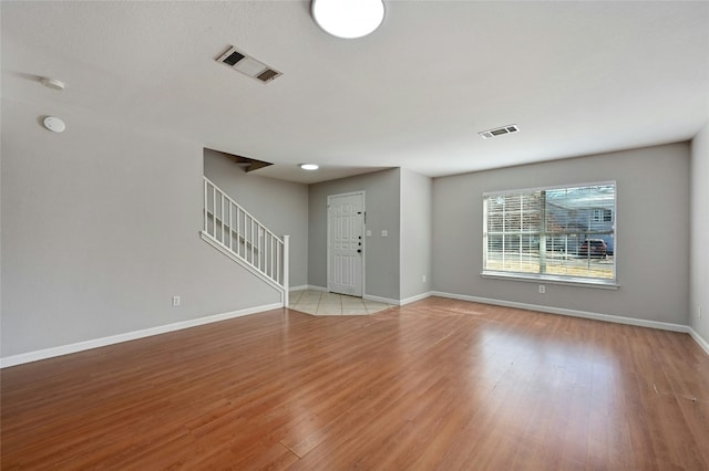 unfurnished living room with light wood-style floors, visible vents, stairway, and baseboards