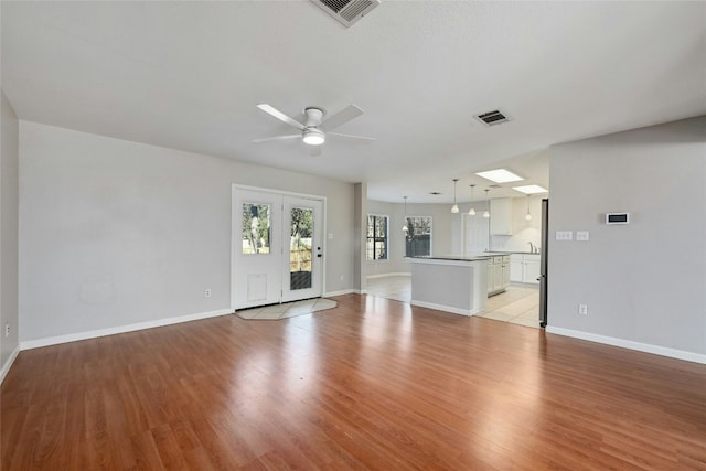 unfurnished living room featuring a skylight, ceiling fan, and light wood-type flooring