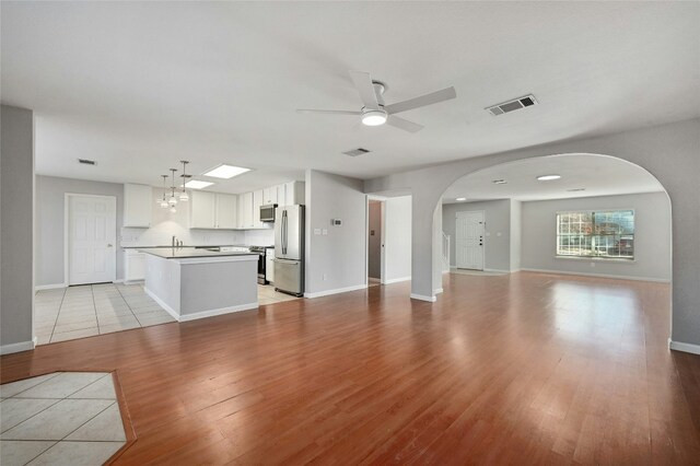 unfurnished living room featuring ceiling fan with notable chandelier, sink, and light hardwood / wood-style floors