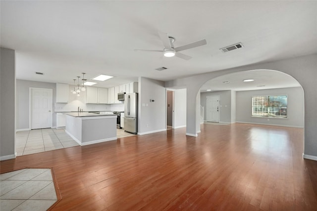 unfurnished living room featuring visible vents, light wood-style flooring, baseboards, and ceiling fan with notable chandelier