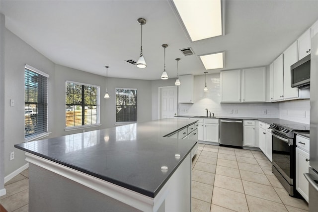 kitchen with hanging light fixtures, a kitchen island, white cabinets, stainless steel appliances, and backsplash