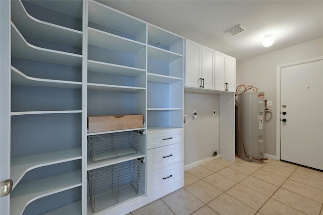 interior space with electric water heater, visible vents, baseboards, and light tile patterned flooring