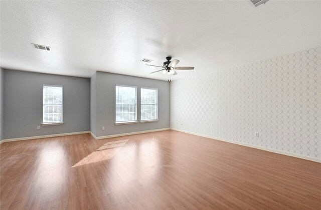 spare room with ceiling fan, a wealth of natural light, a textured ceiling, and light wood-type flooring