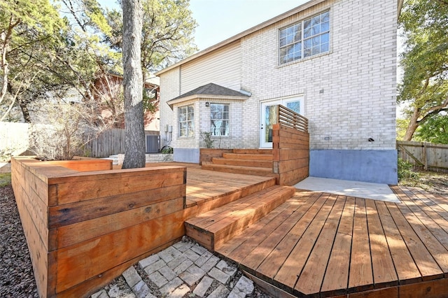 rear view of property featuring brick siding, fence, and a wooden deck