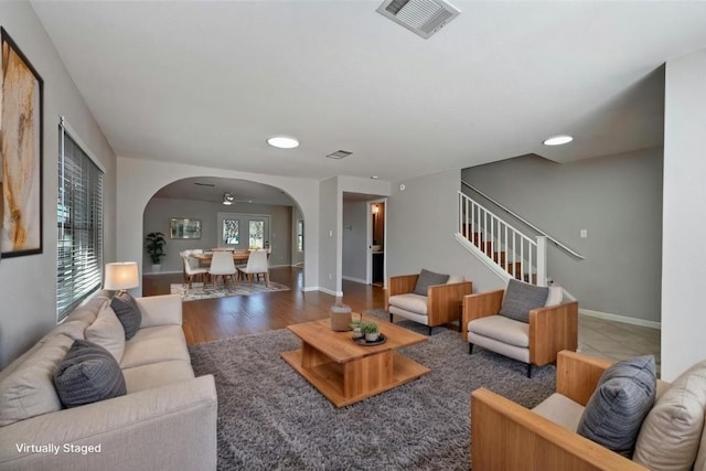 living area with arched walkways, dark wood-type flooring, stairway, and visible vents