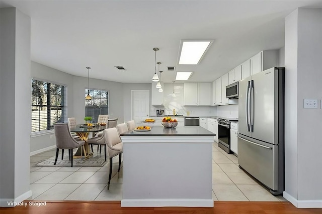 kitchen featuring white cabinets, a kitchen island, appliances with stainless steel finishes, light countertops, and pendant lighting