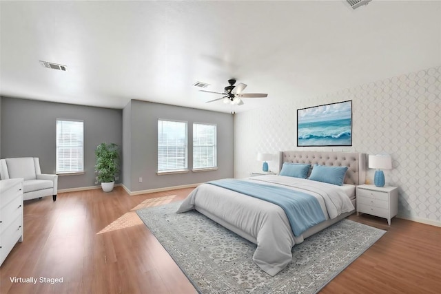 bedroom with wallpapered walls, baseboards, visible vents, and wood finished floors