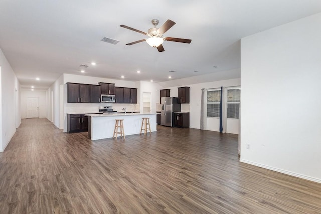 kitchen featuring appliances with stainless steel finishes, dark wood-type flooring, a center island with sink, and a kitchen breakfast bar