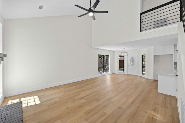 unfurnished living room with ceiling fan, a towering ceiling, and light hardwood / wood-style floors