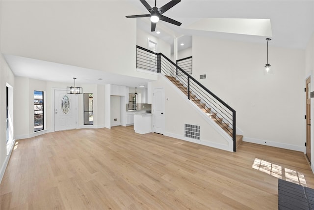 unfurnished living room with a towering ceiling, ceiling fan with notable chandelier, and light hardwood / wood-style flooring