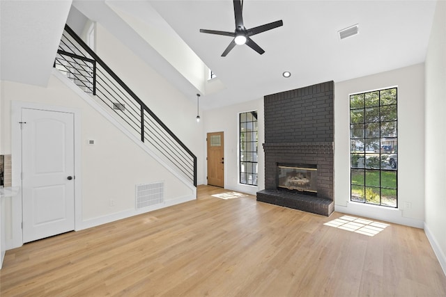 unfurnished living room featuring a brick fireplace, light hardwood / wood-style flooring, ceiling fan, and a high ceiling