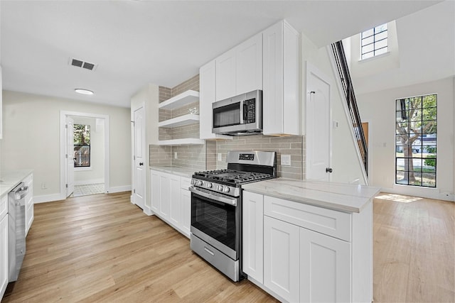 kitchen featuring stainless steel appliances, tasteful backsplash, light stone countertops, and white cabinets