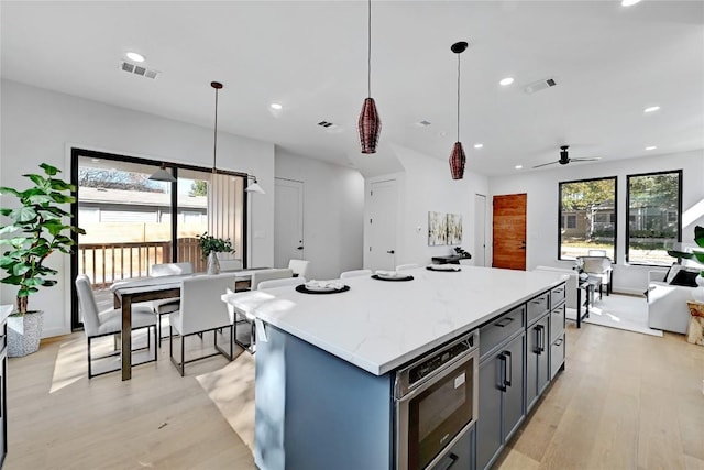 kitchen featuring gray cabinetry, a center island, light wood-type flooring, pendant lighting, and ceiling fan