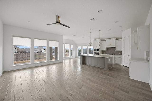 kitchen featuring decorative light fixtures, an island with sink, ceiling fan, decorative backsplash, and white cabinets