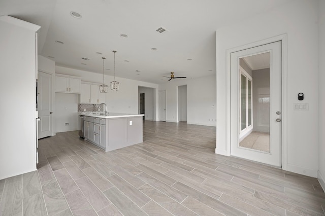 kitchen with sink, white cabinetry, tasteful backsplash, pendant lighting, and a kitchen island with sink