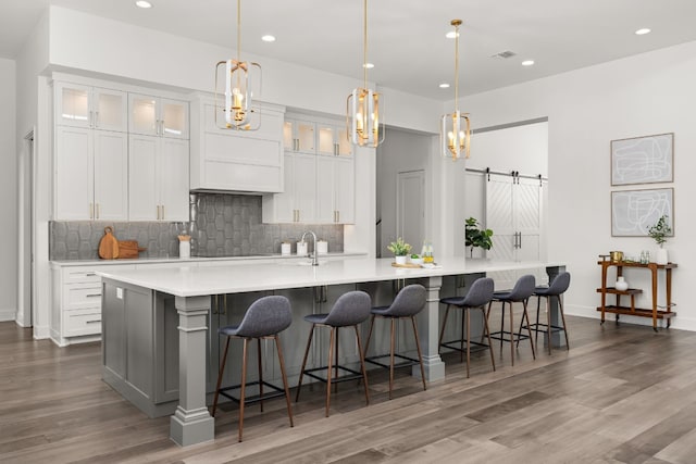 kitchen with white cabinets, hanging light fixtures, a barn door, and a large island with sink