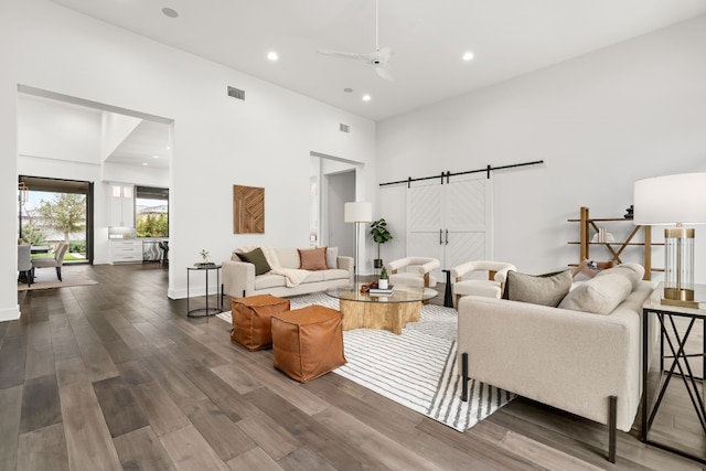 living room with a high ceiling, a barn door, hardwood / wood-style floors, and ceiling fan