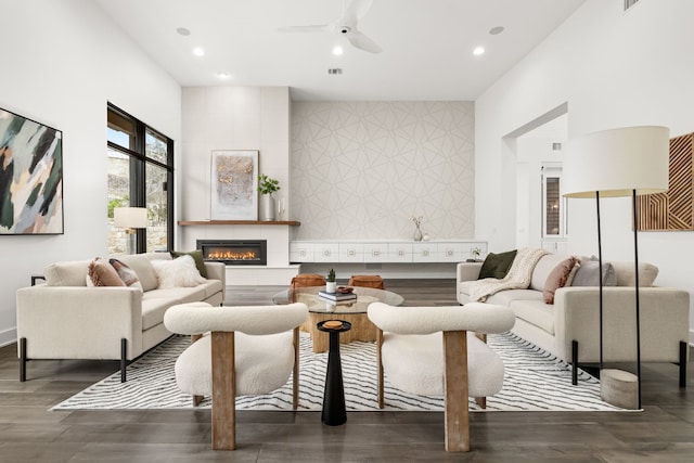 living room with a tiled fireplace, dark wood-type flooring, and ceiling fan