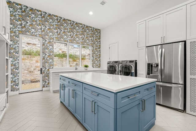 kitchen featuring stainless steel refrigerator with ice dispenser, washing machine and clothes dryer, blue cabinetry, white cabinetry, and a kitchen island