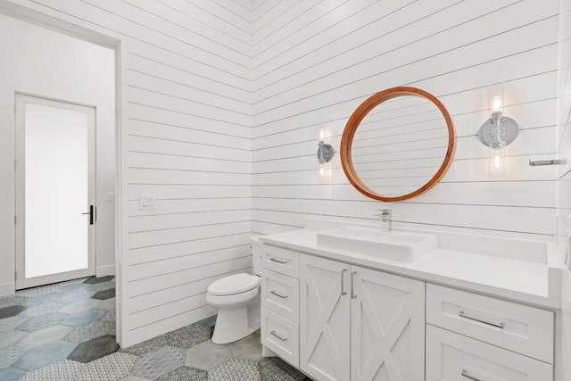 bathroom featuring vanity, toilet, tile patterned floors, and wood walls