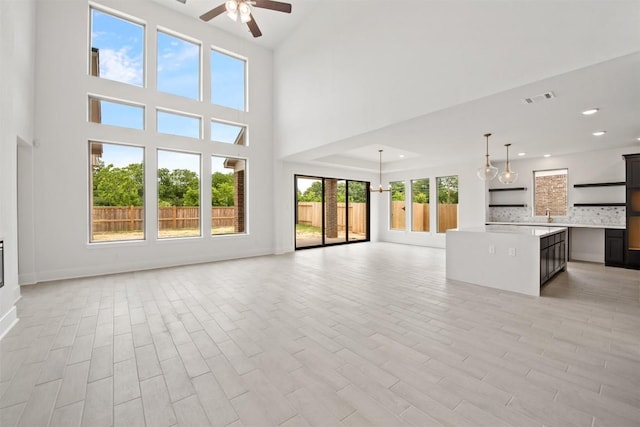 unfurnished living room featuring sink, ceiling fan, and a towering ceiling