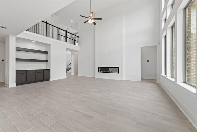 unfurnished living room featuring ceiling fan and a towering ceiling