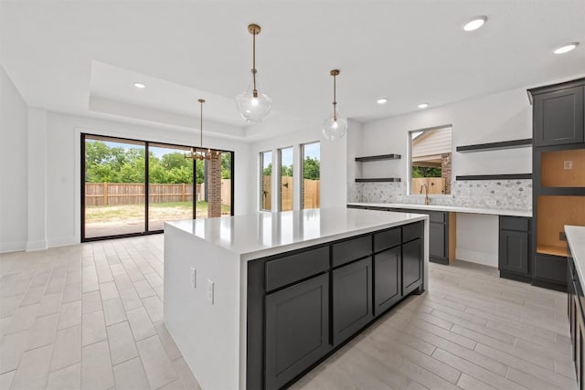 kitchen featuring a raised ceiling, a healthy amount of sunlight, a center island, and decorative backsplash