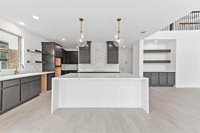 kitchen featuring decorative light fixtures, a center island, decorative backsplash, and light hardwood / wood-style flooring