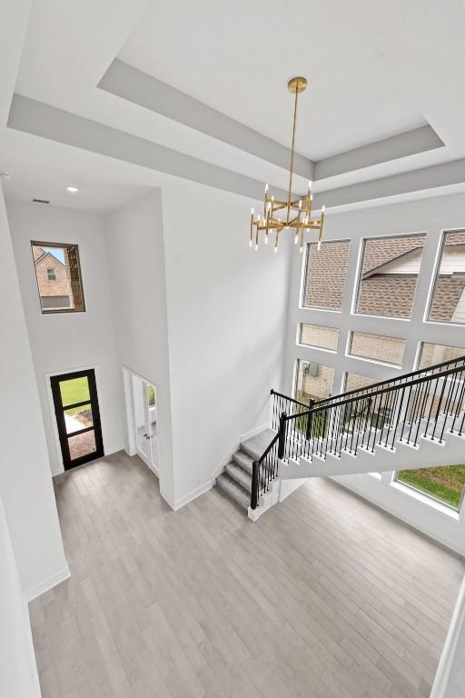 staircase with a healthy amount of sunlight, a tray ceiling, a chandelier, and hardwood / wood-style floors